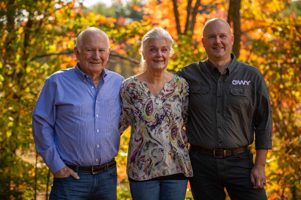 2 men and 1 women taking a picture in front of trees